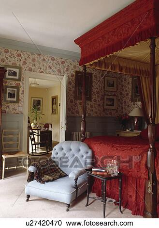 Red silk canopy and cover on antique four-poster bed in country bedroom with pastel blue armchair and floral wallpaper View Large Photo Image Stock Image - Red silk canopy and cover on antique four-poster bed in country bedroom with pastel blue armchair and floral wallpaper. Fotosearch