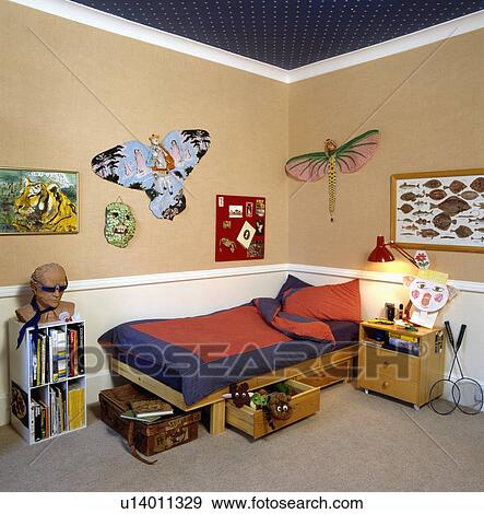 Red+blue pillows and duvet on wooden bed with storage drawers in child's bedroom with paper kites on wall View Large Photo Image Stock Photo - Red+blue pillows and duvet on wooden bed with storage drawers in child's bedroom with paper kites on wall. Fotosearch