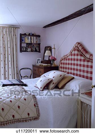 Stock Image - Red+white upholstered headboard on bed with patterned quilt and matching cushions in white cottage bedroom . Fotosearch