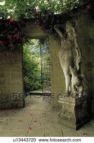 Stock Image - Sculpture beside metal gate in walled garden. Fotosearch