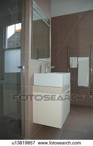 Sideways view of large mirror above wall mounted rectangular basin in modern beige tiled bathroom View Large Photo Image Stock Photo - Sideways view of large mirror above wall mounted rectangular basin in modern beige tiled bathroom. Fotosearch