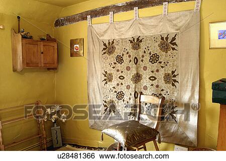 Stock Photograph - Silk-edged wall-hanging in yellow bedroom with small pine wall cabinet. Fotosearch