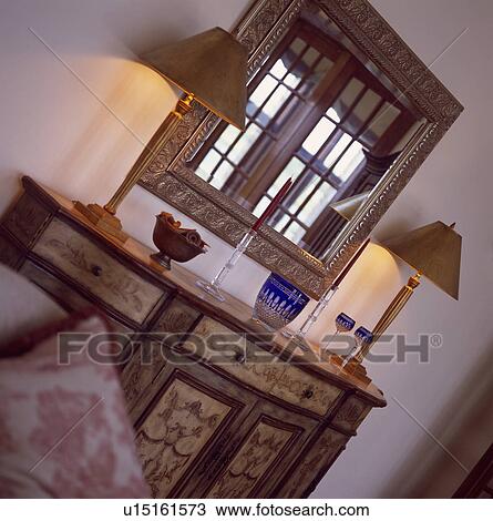 Slanted view of mirror above antique painted cupboard with lighted lamps with brown shades View Large Photo Image Stock Image - Slanted view of mirror above antique painted cupboard with lighted lamps with brown shades. Fotosearch