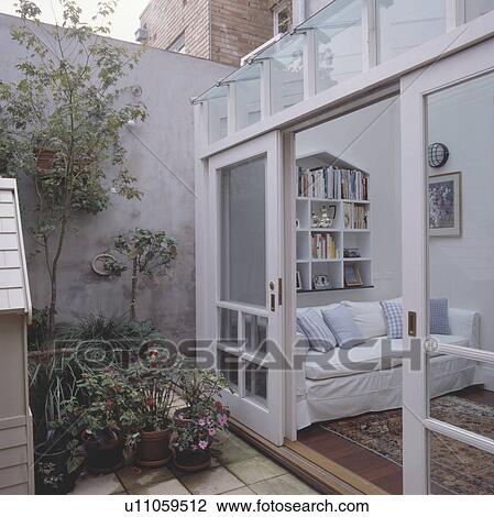 Stock Image - Small enclosed patio outside modern conservatory extension with open sliding glazed doors. Fotosearch