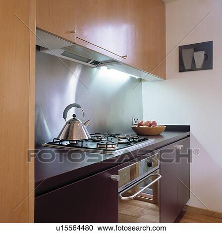 Stock Image - Small modern kitchen with wooden units and stainless splashback. Fotosearch
