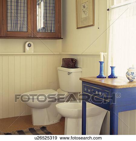 Small painted blue table beside bidet and toilet in cream bathroom with panelling to dado height View Large Photo Image Stock Photo - Small painted blue table beside bidet and toilet in cream bathroom with panelling to dado height. Fotosearch