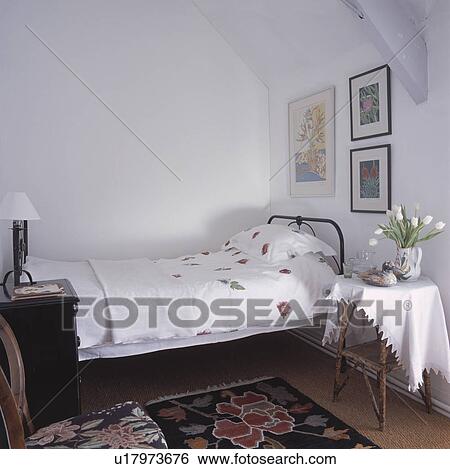 Small traditional white bedroom with black bed frame and cane side table View Large Photo Image Stock Photograph - Small traditional white bedroom with black bed frame and cane side table . Fotosearch