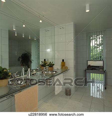 Stock Photograph - Stainless steel basins in glass vanity shelf in modern white tiled bathroom with white tiled floor. Fotosearch