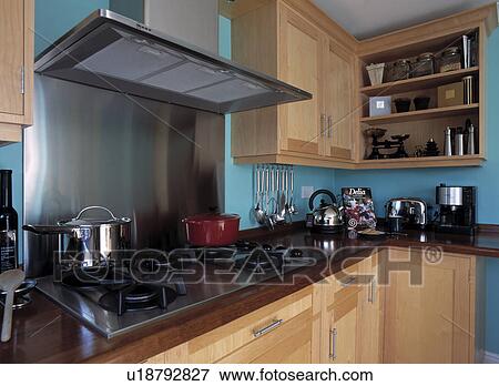 Stock Photo - Stainless steel extractor fan above hob in blue kitchen with pale wood fitted cupboards. Fotosearch