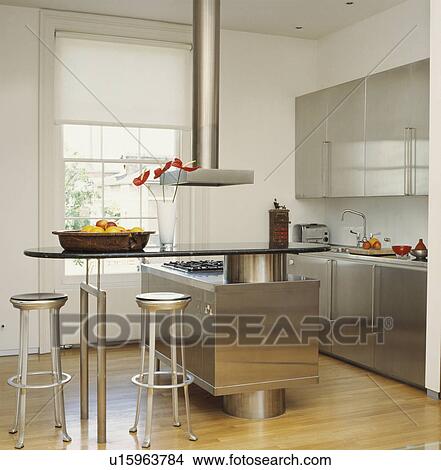 Picture - Stainless steel fitted cupboards in modern kitchen with wooden flooring and metal stools at breakfast bar. Fotosearch