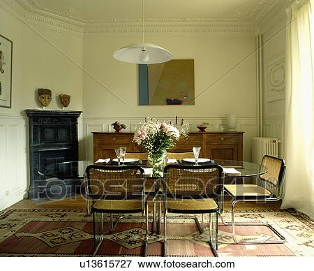 Steel and cane cantilevered chairs and glass table in dining room with black cast-iron fireplace and patterned rug View Large Photo Image Stock Photo - Steel and cane cantilevered chairs and glass table in dining room with black cast-iron fireplace and patterned rug. Fotosearch