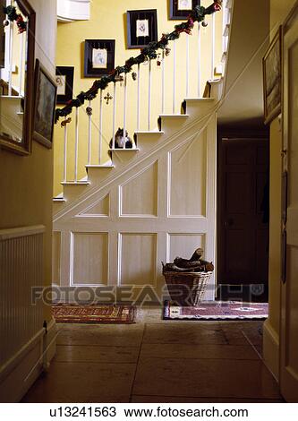 Stock Image - Stone flagged floor in large country hall with white panelled wall and garland on bannisters. Fotosearch