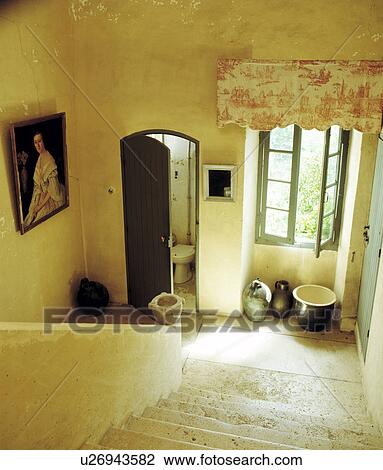 Stock Image - Stone staircase and small landing with pink Toile-de-Jouy drape above window beside door open to toilet . Fotosearch