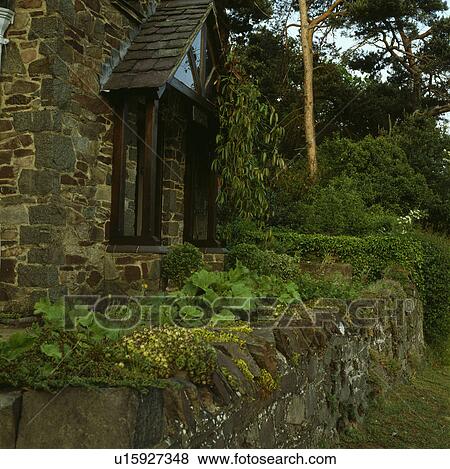Stock Photo - Stone wall in front of stone cottage. Fotosearch