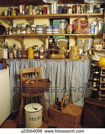 Stock Photo - Storage jars on wooden shelves above scales on worktop with curtain in larder with baskets and wooden chair. Fotosearch