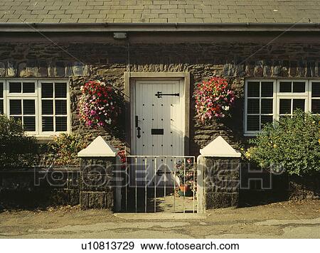 Stock Photo - Summer flowering annuals in hanging baskets on either side of white front door in stone cottage. Fotosearch