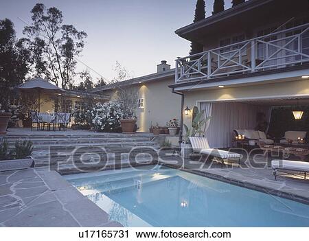 Swimmingpool beside house with balcony above loungers and steps up to patio View Large Photo Image Stock Image - Swimmingpool beside house with balcony above loungers and steps up to patio . Fotosearch