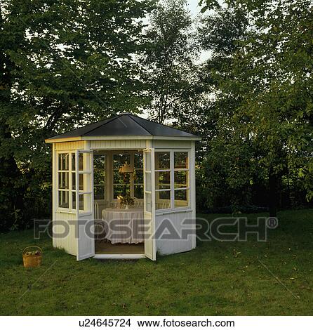 Table laid for dinner in white wooden summerhouse in large country garden in summer View Large Photo Image Picture - Table laid for dinner in white wooden summerhouse in large country garden in summer. Fotosearch