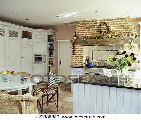 Stock Photo - Table with assorted chairs in country kitchen with island unit and brick fireplace. Fotosearch