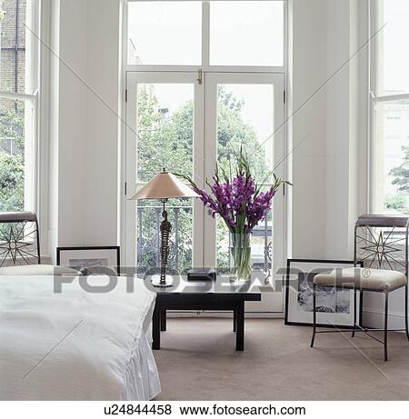 Tall lamp and purple gladioli on low table in front of French windows in white contemporary bedroom with cream carpet View Large Photo Image Stock Photo - Tall lamp and purple gladioli on low table in front of French windows in white contemporary bedroom with cream carpet. Fotosearch