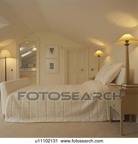 Tall lighted lamps on either side of cream upholstered bed with cream quilt in modern cream loft conversion bedroom View Large Photo Image Stock Image - Tall lighted lamps on either side of cream upholstered bed with cream quilt in modern cream loft conversion bedroom. Fotosearch