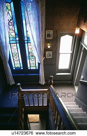 Stock Photograph - Tall stained glass window and white curtains on traditional landing with grey carpet. Fotosearch