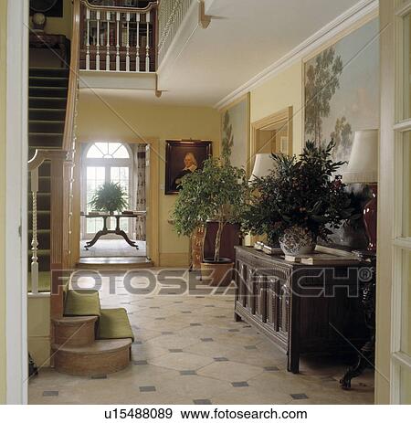 Stock Photo - Tiled floor and antique carved chest in large neutral country hall with houseplants and pictures. Fotosearch
