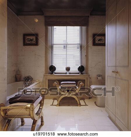 Towels on gilt stools in modern bathroom with marble wall tiles and white ceramic floor tiles View Large Photo Image Stock Photo - Towels on gilt stools in modern bathroom with marble wall tiles and white ceramic floor tiles. Fotosearch