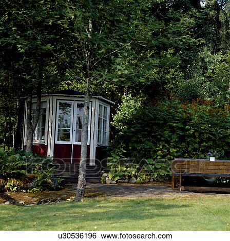 Stock Photograph - Tree on lawn in front of white summerhouse in country garden in summer. Fotosearch