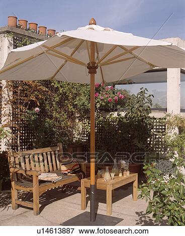 Stock Photo - Umbrella and wooden furniture on small town roof garden in summer. Fotosearch