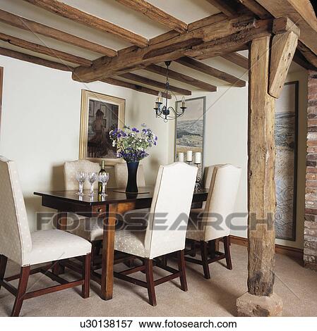 Stock Photo - Upholstered cream chairs with high backs in neutral cottage living room with upright beam and beamed ceiling . Fotosearch