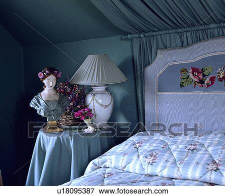 Stock Photo - Upholstered floral headboard on bed with blue+white striped and floral quilt in bedroom with bust and lamp on table. Fotosearch