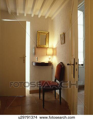 Picture - Upholstered red chair and lighted lamp on shelf in small white hall with beamed white ceiling . Fotosearch