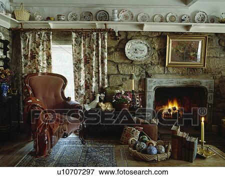 Victorian armchair beside fire in livingroom with plateshelf above stone walls and floral curtains View Large Photo Image Stock Photo - Victorian armchair beside fire in livingroom with plateshelf above stone walls and floral curtains. Fotosearch
