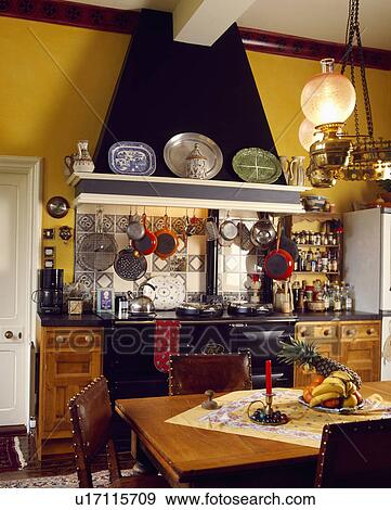 Stock Photo - Victorian lamp above table and chairs in traditional kitchen with black Aga and apex ceiling . Fotosearch