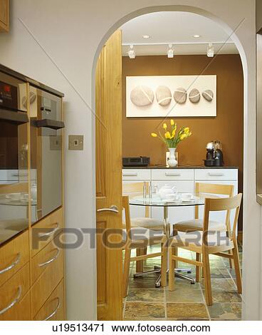 Stock Image - View through arched doorway to modern table and chairs in dining room with picture above sideboard. Fotosearch