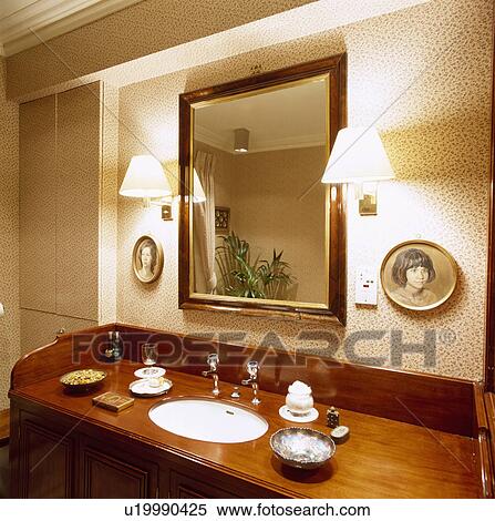 Wall-lights on either side of mirror above basin in wood vanity unit View Large Photo Image Stock Photography - Wall-lights on either side of mirror above basin in wood vanity unit . Fotosearch