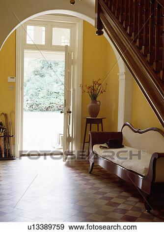 Stock Photo - White 19th century sofa in traditional country hall with brown and cream tiled floor and open front door. Fotosearch