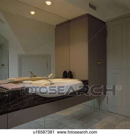 White Basin Built Into Brown Vanity Unit Below Mirrored Wall In Modern Bathroom Stock Image U16587381 Fotosearch