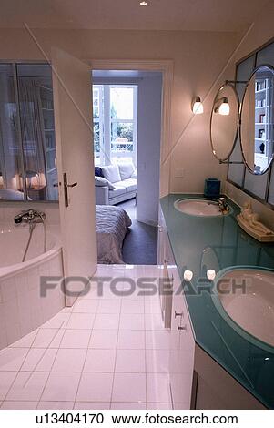 White basins in vanity unit with glass top in modern white bathroom with white floor tiles and door open to bedroom View Large Photo Image Stock Image - White basins in vanity unit with glass top in modern white bathroom with white floor tiles and door open to bedroom . Fotosearch