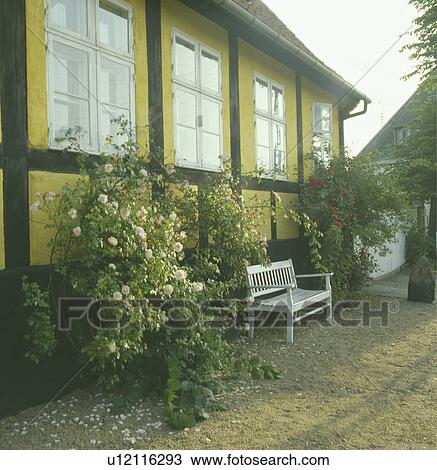 Stock Image - White bench in front of yellow country house in Germany. Fotosearch