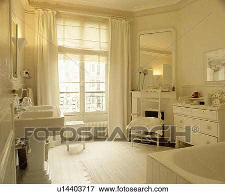 Stock Photo - White blind and curtains on window in white bathroom with white chest of drawers and mirror above fireplace. Fotosearch