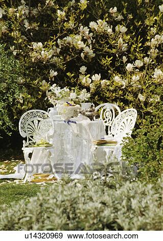 Stock Photo - White chairs and cloth on table in country garden in summer. Fotosearch