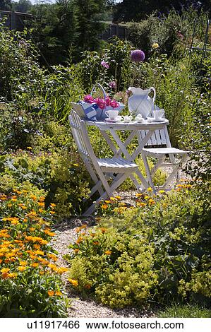 Stock Photograph - White chairs and table with white jug in country garden in summer. Fotosearch