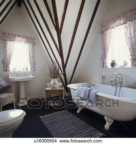 Picture - White clawfoot bath in white attic bathoom with beamed walls and apex ceiling. Fotosearch