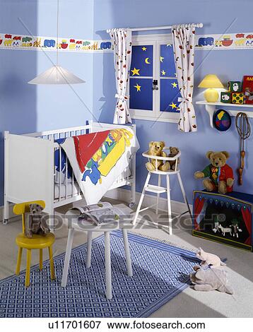 Stock Photo - White cot and table in pastel blue nursery bedroom with blue rug and brightly patterned wallpaper border. Fotosearch