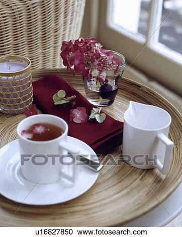 Stock Image - White cup and saucer with white jug on circular wooden tray with pink hydrangea in glass. Fotosearch