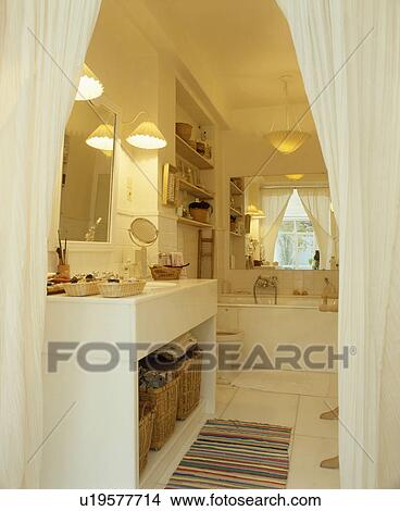 White curtains open to white bathroom with wall lights on either side of basin in white unit above storage baskets View Large Photo Image Picture - White curtains open to white bathroom with wall lights on either side of basin in white unit above storage baskets. Fotosearch