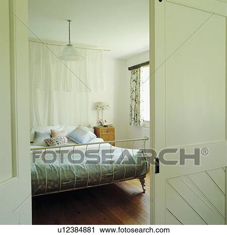 White doors open to bedroom with white drapes behind antique white metal bed and wooden floor View Large Photo Image Stock Image - White doors open to bedroom with white drapes behind antique white metal bed and wooden floor. Fotosearch