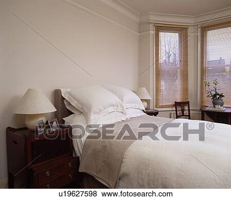 White pillows and linen on bed in cream bedroom with slatted wooden blinds on bay window View Large Photo Image Stock Photo - White pillows and linen on bed in cream bedroom with slatted wooden blinds on bay window. Fotosearch